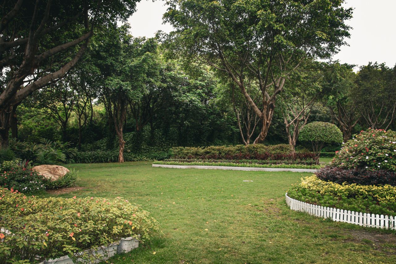 Services A serene garden with trees, flower beds, and manicured lawns surrounded by greenery.
